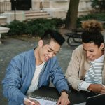 Two college students studying and discussing notes outdoors, smiling and engaged.